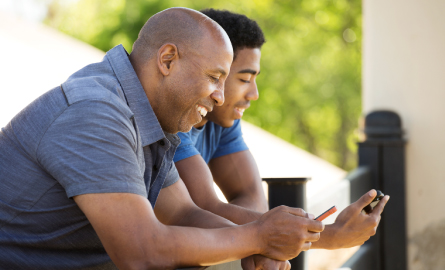 A father and son looking at their cellphones smiling. 
